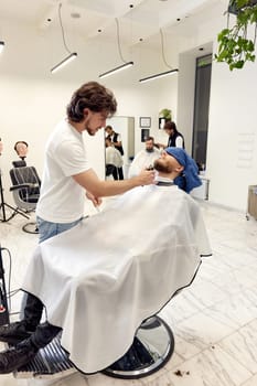 Barber shaving handsome bearded man in barber shop.