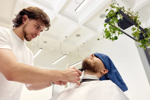 Barber shaving handsome bearded man in barber shop.
