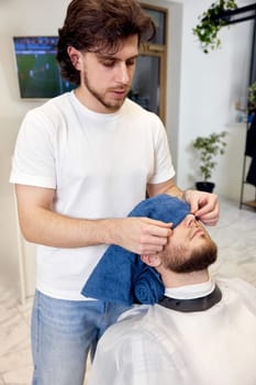 Barber shaving handsome bearded man in barber shop.