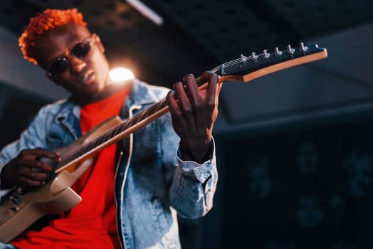 Plays guitar. Young african american performer rehearsing in a recording studio.