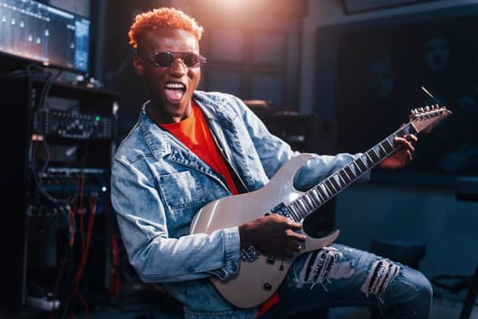 Plays guitar. Young african american performer rehearsing in a recording studio.