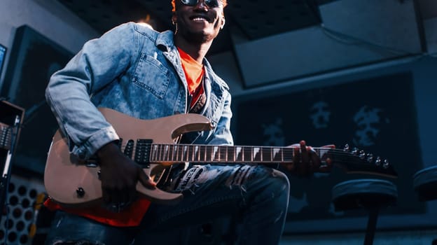 Plays guitar. Young african american performer rehearsing in a recording studio.