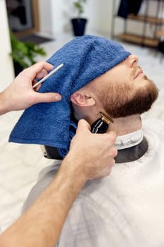 Barber shaving handsome bearded man in barber shop.