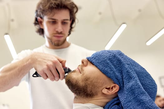 Barber shaving handsome bearded man in barber shop.