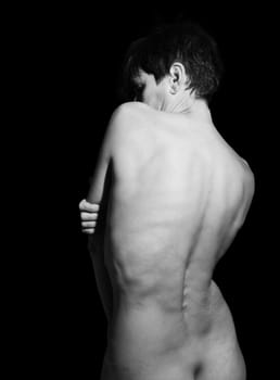 Black and white of back view of unrecognizable naked fit woman with short dark hair standing in studio with crossed arms