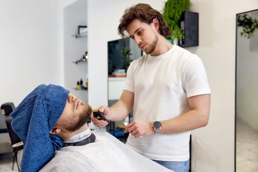 Barber shaving handsome bearded man in barber shop.