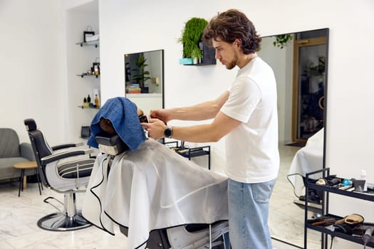 Barber shaving handsome bearded man in barber shop.