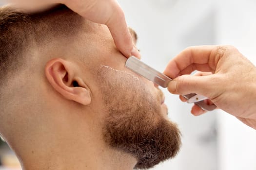 Barber shaving bearded man with retro knife in barber shop. close-up