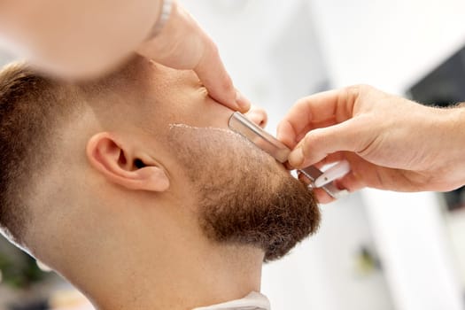 Barber shaving bearded man with retro knife in barber shop. close-up