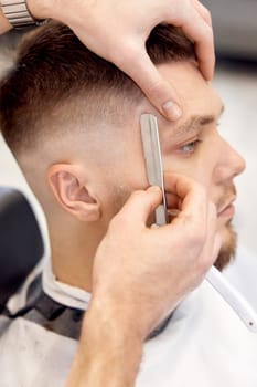 Barber shaving bearded man with retro knife in barber shop. close-up