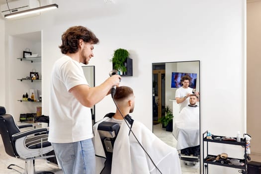 Professional hairdresser during work with man client with hair dryer in barber shop. Haircut in the barbershop.