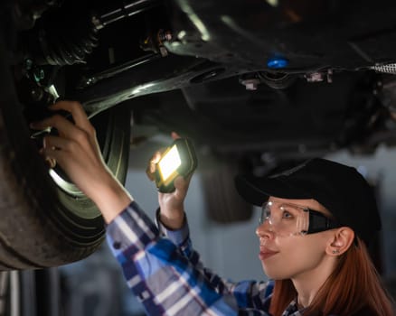 A female mechanic inspects a lifted car. A girl at a man's work