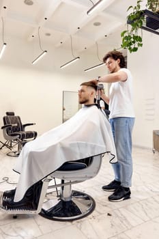 Professional hairdresser during work with man client with hair dryer in barber shop. Haircut in the barbershop.