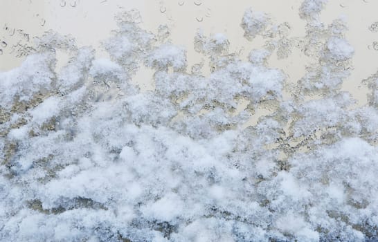 Image of melting snow on the glass of a large window.