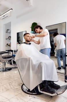 Hairstylist serving handsome bearded man in barber shop.