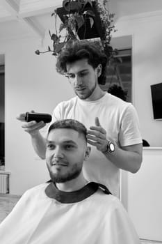 Hairstylist serving handsome bearded man in barber shop.