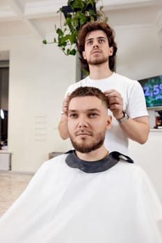 Barber and satisfied bearded man in front of the mirror in barber shop