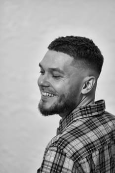 happy young man with stylish hair and beard in a plaid shirt on gray background. black and white