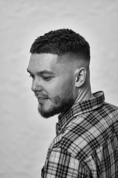 happy young man with stylish hair and beard in a plaid shirt on gray background. black and white