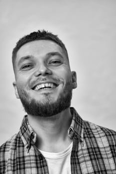 happy young man with stylish hair and beard in a plaid shirt on gray background. black and white