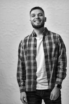 happy young man with stylish hair and beard in a plaid shirt on gray background. black and white