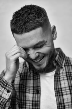 happy laughing young man with stylish hair and beard in a plaid shirt on gray background. black and white
