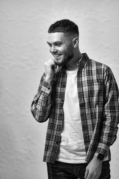 laughing young man with stylish hair and beard in a plaid shirt on gray background. black and white