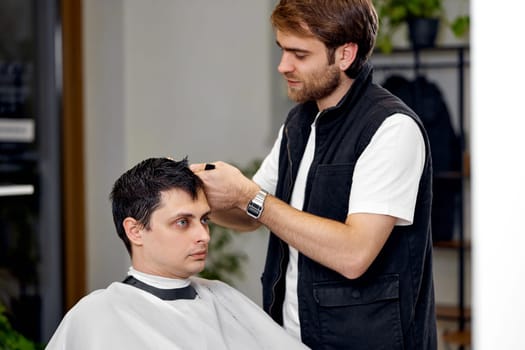 young caucasian man getting haircut by professional male hairstylist at barber shop.