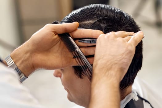 close-up, professional hairstylist does haircut for caucasian client man at barber shop.