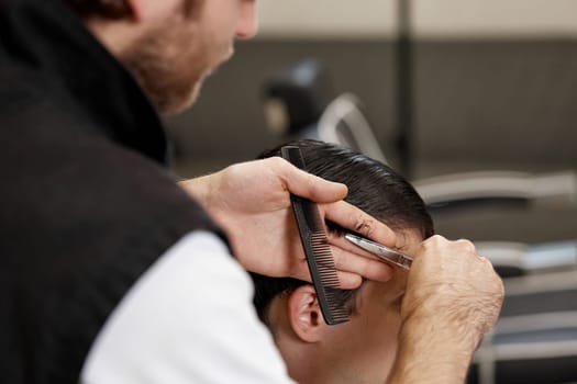 close-up, professional hairstylist does haircut for caucasian client man at barber shop.