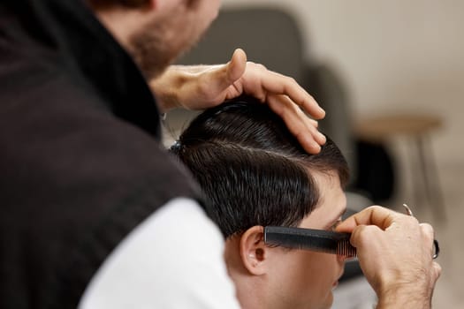 close-up, professional hairstylist does haircut for caucasian client man at barber shop.