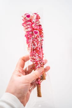 Chocolate-covered pretzel rods decorated with heart-shaped sprinkles for Valentine's Day packaged in a clear bags.