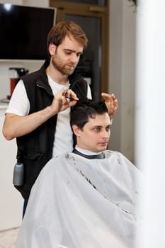 Professional hairdresser does haircut for caucasian client man at barber shop.