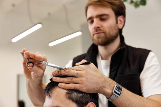 Professional hairdresser does haircut for caucasian client man at barber shop.