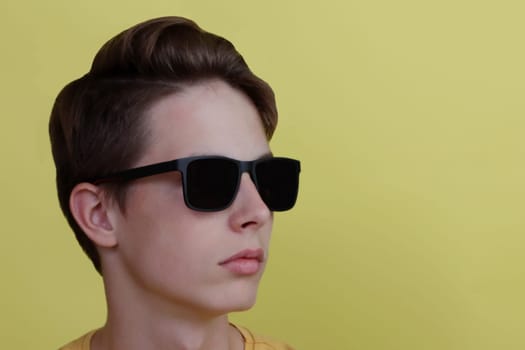 Close-up portrait of an attractive boy 14-17 years old in glasses on a yellow background.