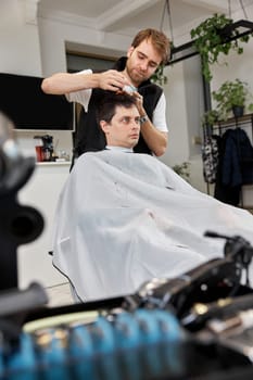Hairstylist serving handsome caucasian man in barber shop.