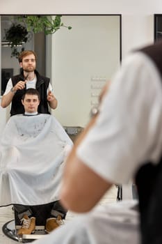 Hairstylist serving handsome caucasian man in barber shop.