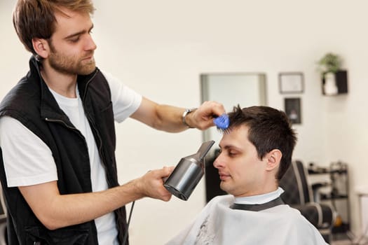 Professional hairdresser during work with man client with hair dryer in barber shop. Haircut in the barbershop.