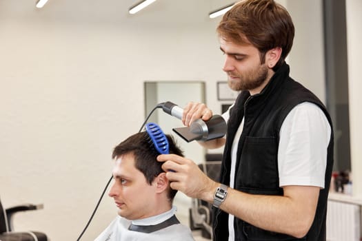 Professional hairdresser during work with man client with hair dryer in barber shop. Haircut in the barbershop.