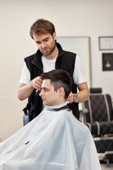 Barber shaving handsome caucasian man in barber shop.