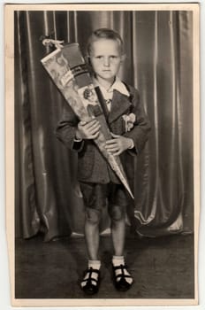 GERMANY - CIRCA 1940s: Vintage photo shows pupil boy with Schultute or School Cone, sweets for the first day in school. Studio photo with sepia tint. Black and white retro image.