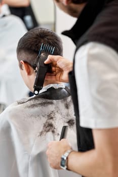 Barber cut hair with electric shearer machine on man in barber shop.