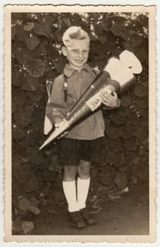 GERMANY- CIRCA 1940s: Vintage photo shows pupil boy with Schultute or School Cone, sweets for the first day in school. Studio photo with sepia tint. Black and white retro image.