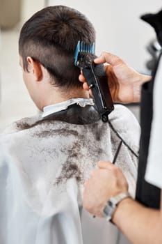 Barber trim hair with clipper on handsome man in barber shop.