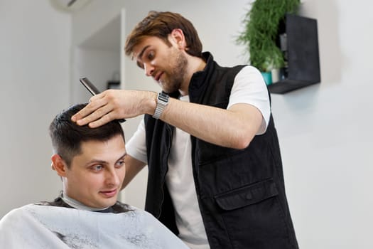 Barber trim hair with clipper on handsome man in barber shop.