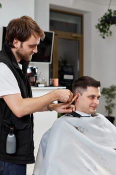 Barber cut hair with electric shearer machine on man in barber shop.