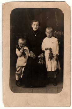 GERMANY - CIRCA 1930s: Vintage photo shows woman and her children in a photography studio. Boy wears a sailor costume and girl white dress. Retro black and white studio photography with sepia effect.