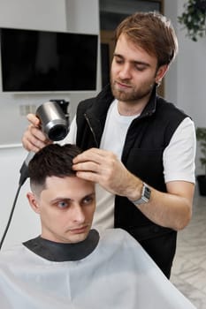bearded barber during work with man client with hair dryer in barber shop. Haircut in the barbershop.