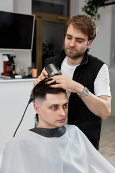 barber during work with man client with hair dryer in barber shop. Haircut in the barbershop.