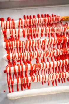 Drizzling melted chocolate over chocolate-dipped pretzels rods and decorating with sprinkles to make chocolate-covered pretzel rods for Valentine's Day.